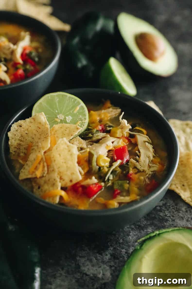 A vibrant bowl of chicken poblano soup garnished with tortilla chips, a fresh lime wedge, and shredded cheese.