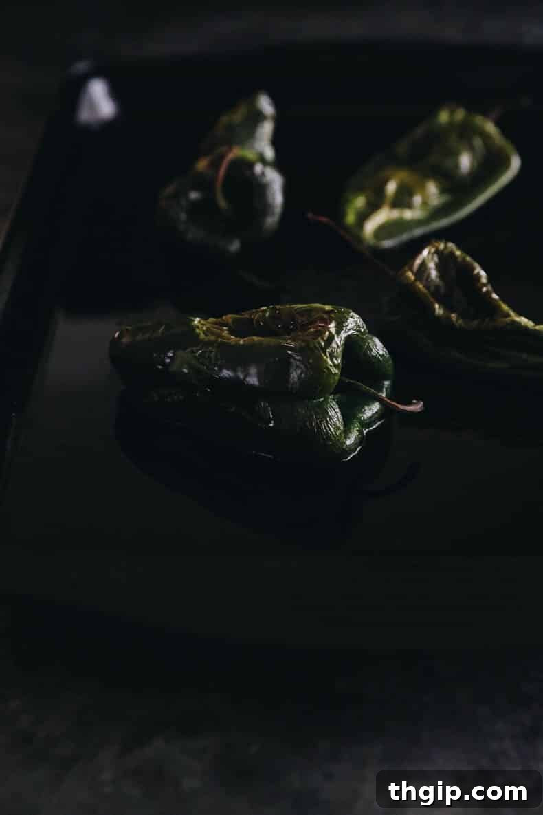 Roasted poblano peppers cooling on a baking sheet, showing their charred and softened skins.