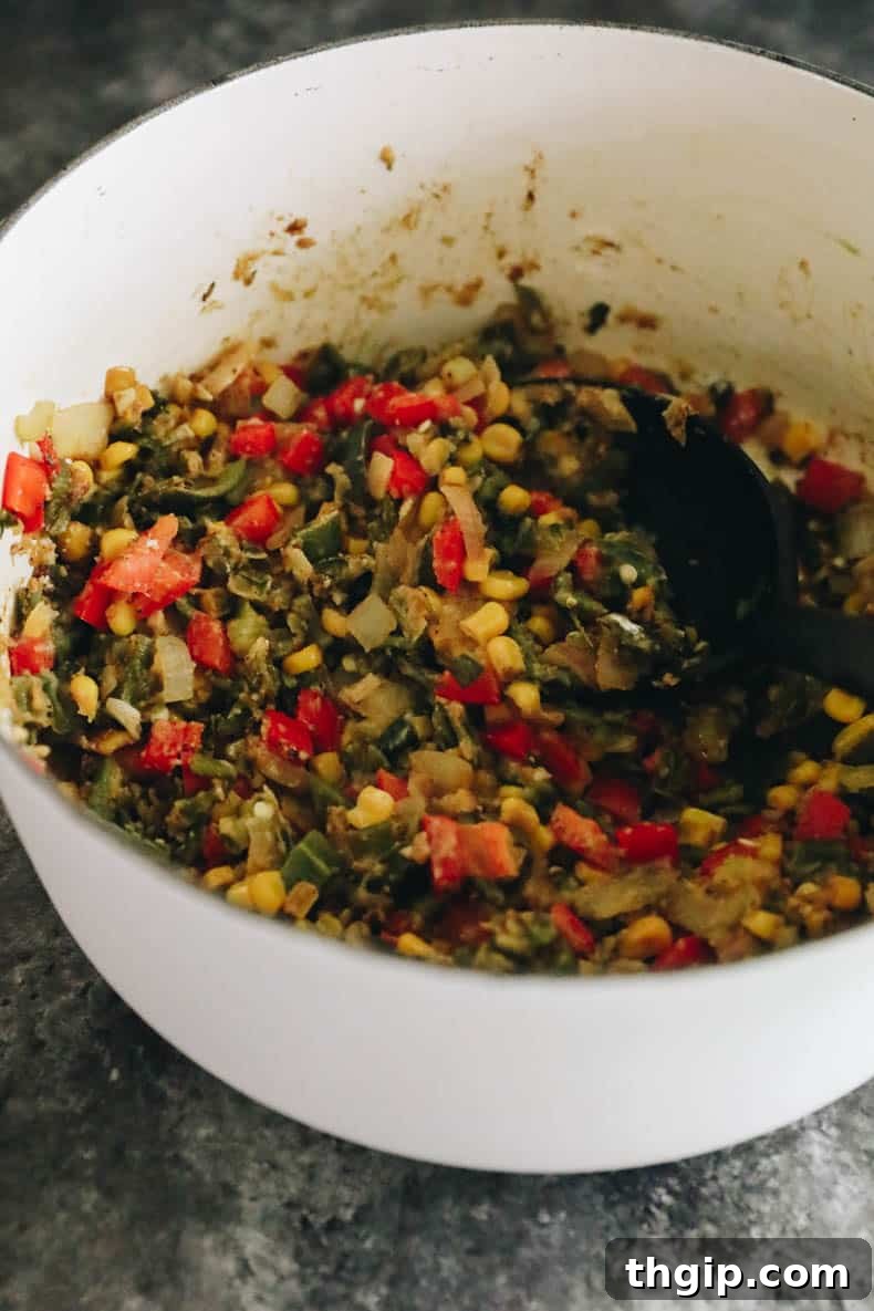 The savory base for chicken poblano soup, featuring sautéed vegetables and spices, simmering in a white Dutch oven.