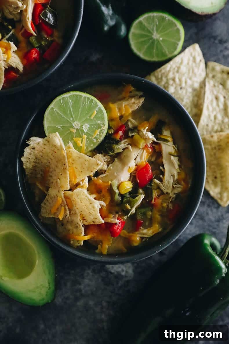 An overhead shot of a blue bowl filled with chicken poblano soup, generously topped with crunchy tortilla chips, shredded cheese, and a vibrant lime wedge.
