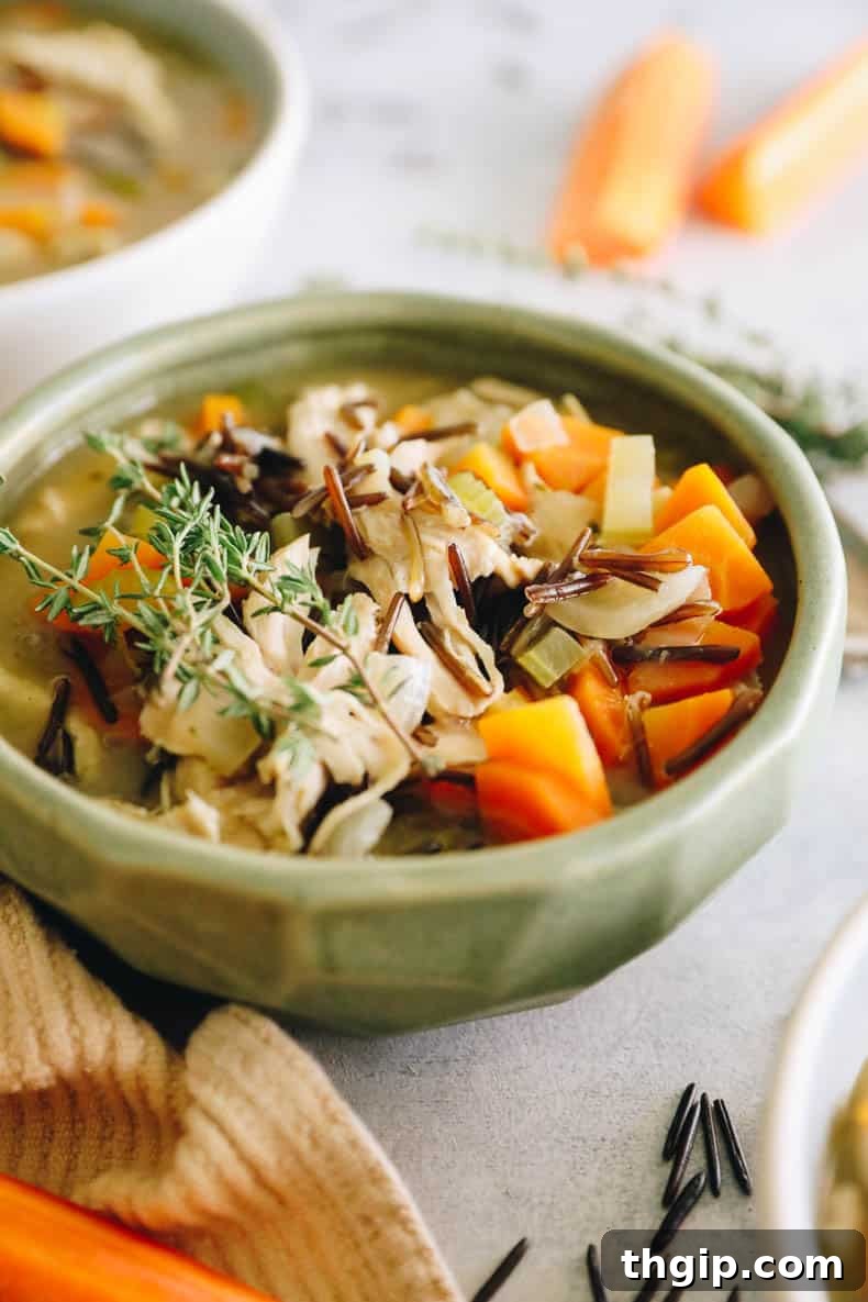 Creamy Chicken Wild Rice Delight 2 A beautiful green ceramic bowl filled generously with rich and creamy chicken and wild rice soup, elegantly topped with fresh thyme sprigs.