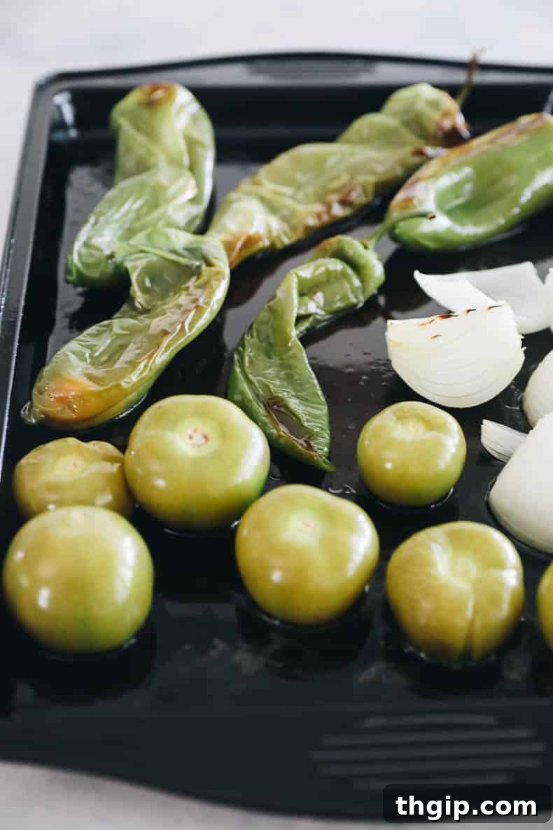 Zesty Green Enchilada Sauce 4 roasted hatch peppers, tomatillos and onion on a baking sheet.