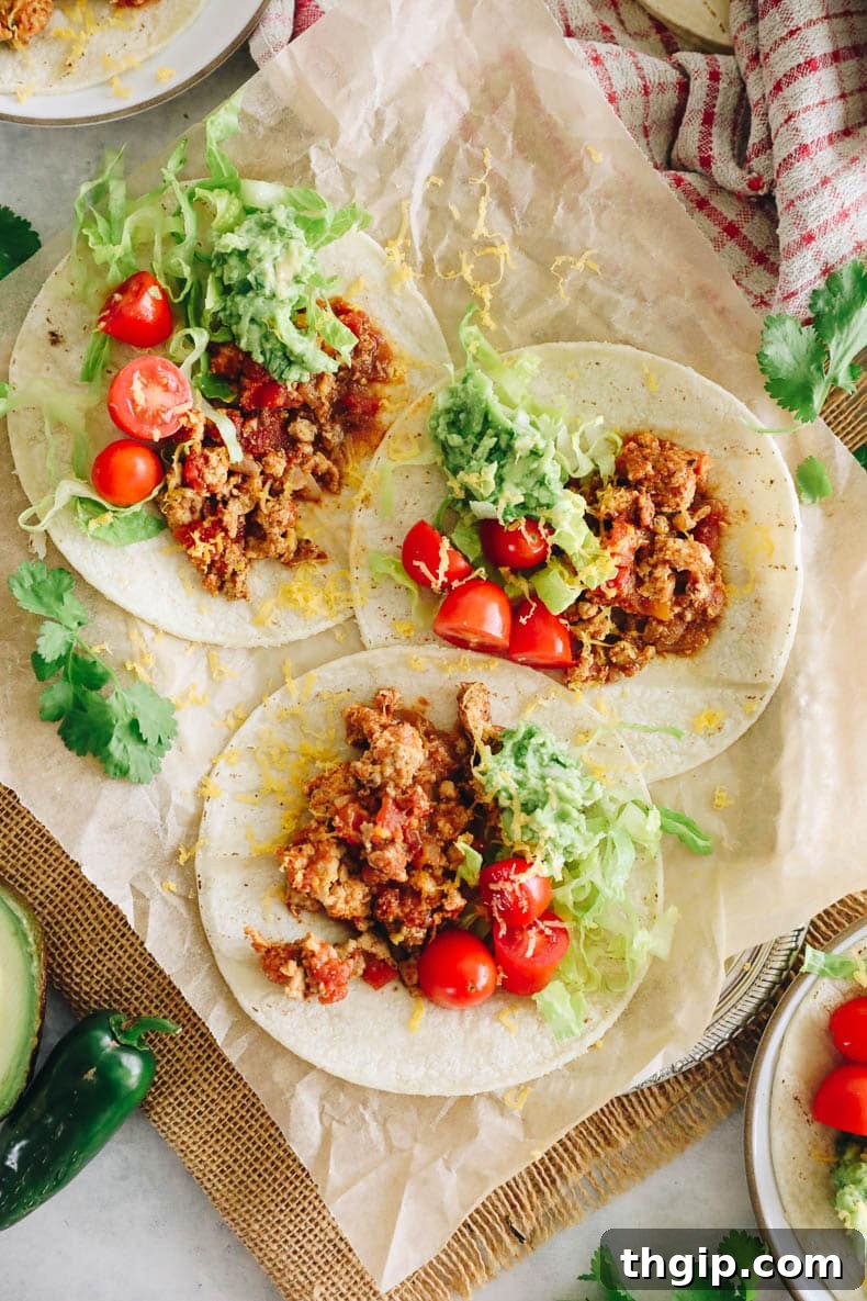Zesty Turkey Tacos 7 Overhead view of multiple fresh turkey tacos beautifully arranged on a parchment-lined plate, garnished with tomatoes, guacamole, and shredded lettuce.