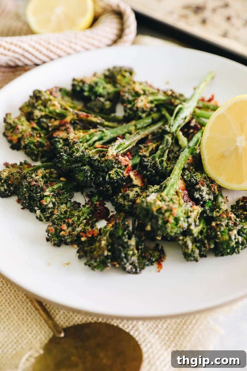 Golden Roasted Broccolini 2 Roasted broccolini on a white plate sprinkled with parmesan and a sliced lemon.