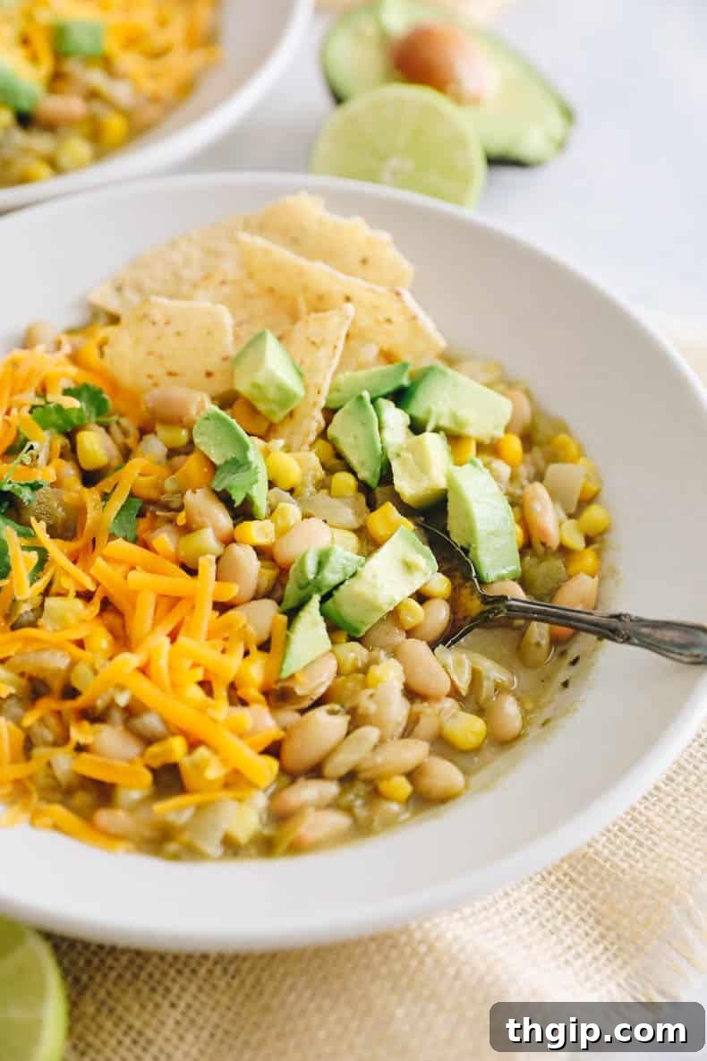 Creamy White Bean Chili 6 A beautifully presented bowl of white bean chili, generously topped with avocado, shredded cheese, fresh cilantro, and crispy tortilla chips.