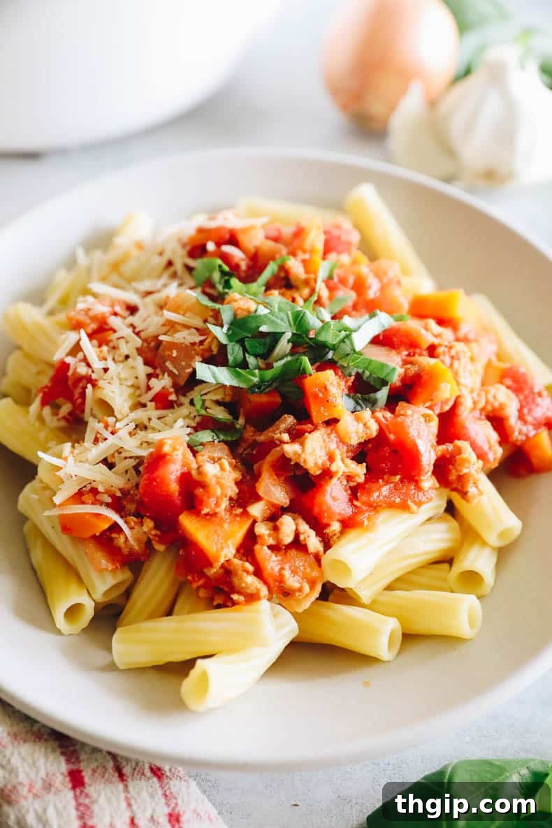 turkey bolognese on a bed of rigatoni noodles in a white bowl.