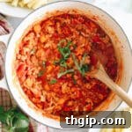 overhead image of turkey bolognese in a white dutch oven sprinkled with basil and a wooden spoon.