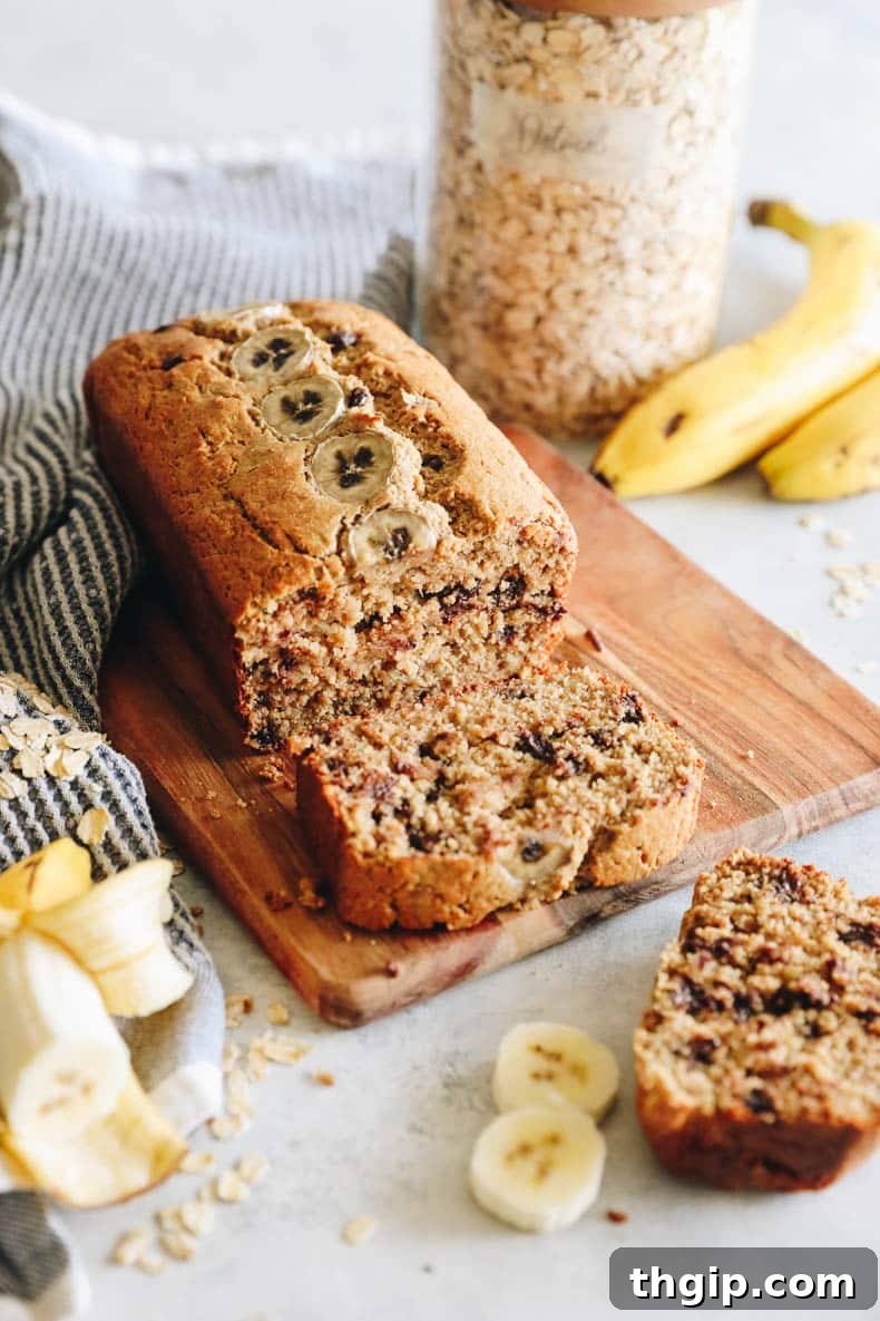 Golden Oat Flour Banana Bread 2 Golden-brown oat flour banana bread on a rustic cutting board, adorned with melted chocolate chips and fresh banana slices, ready to be enjoyed.