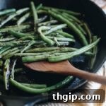 Close up of charred green beans on a white plate, garnished with pomegranate seeds and fresh herbs