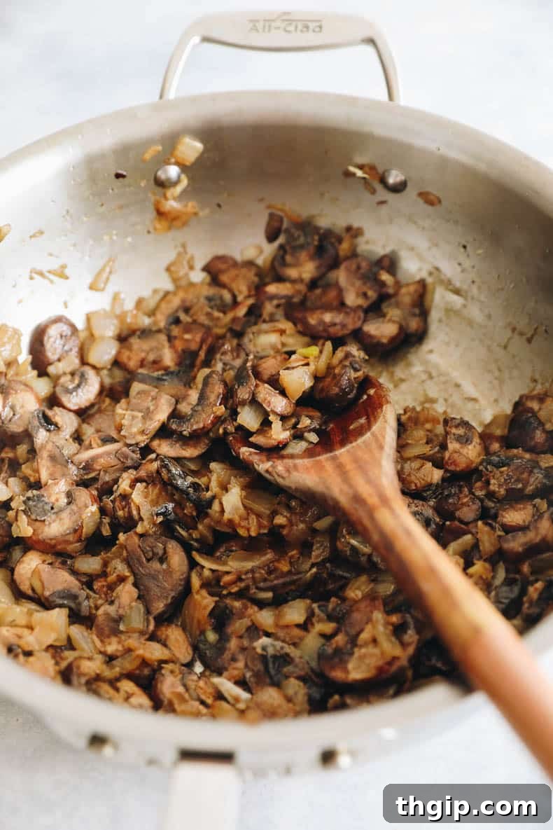Mushrooms and onions sautéing in a large pan, beginning to brown and release their moisture, forming the base of the mushroom stroganoff.