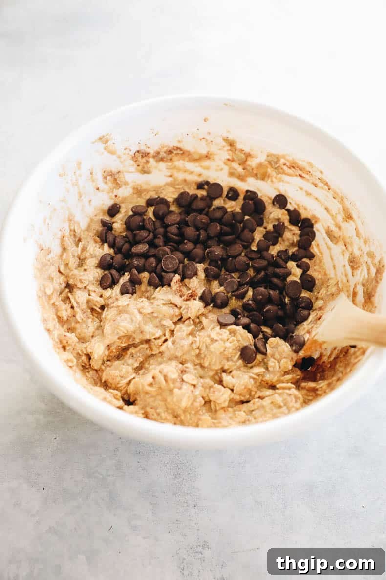 chocolate chips being mixed into oatmeal bar batter in a white bowl.