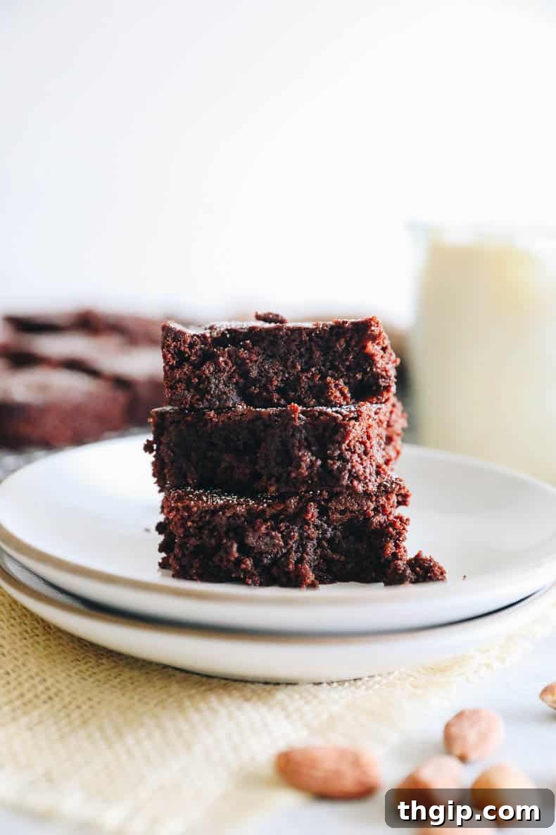 3 almond flour brownies stacked on a white plate, showcasing their fudgy texture and crinkly tops.