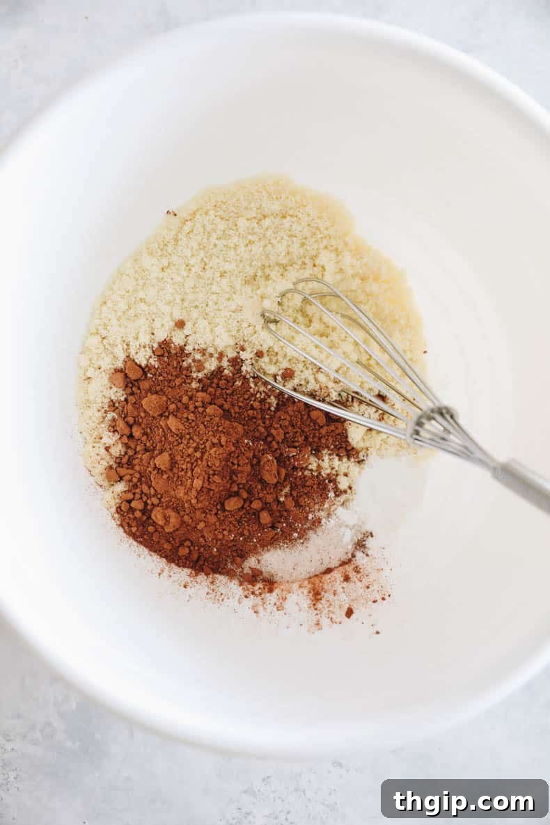 Dry ingredients for almond flour brownies in a white bowl with a whisk, ready for mixing.