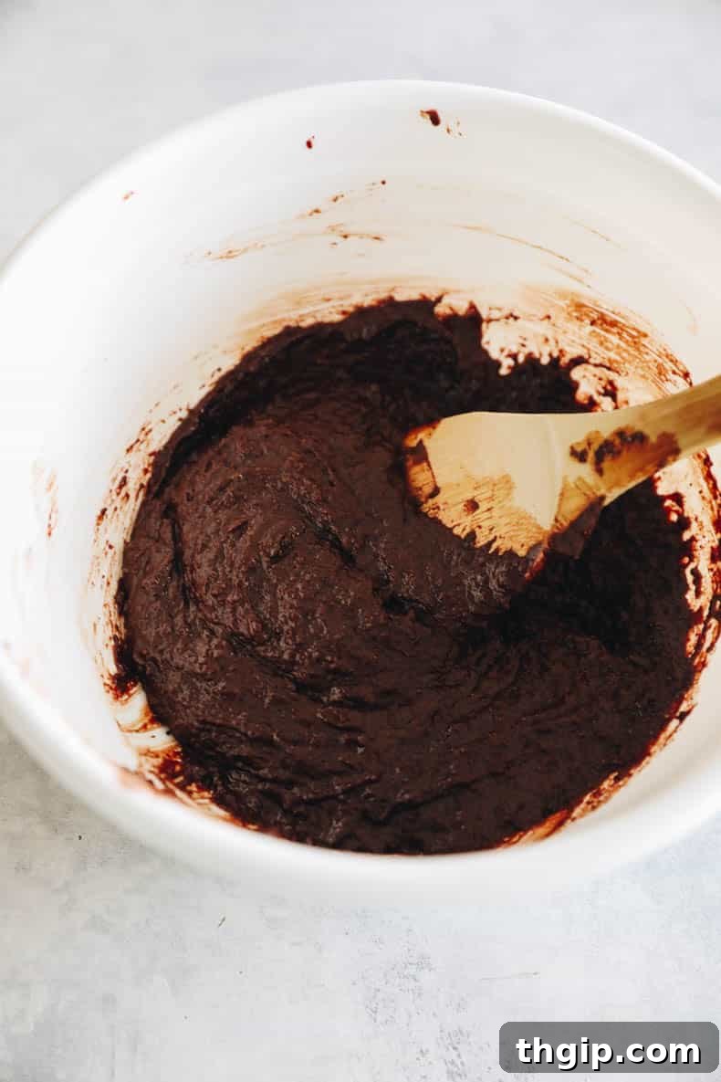 Almond flour brownie batter in a white bowl with a wooden spoon, showing its rich, thick consistency.
