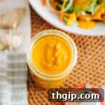 Ginger salad dressing stored in a mason jar with a dressed salad in a shallow white bowl.