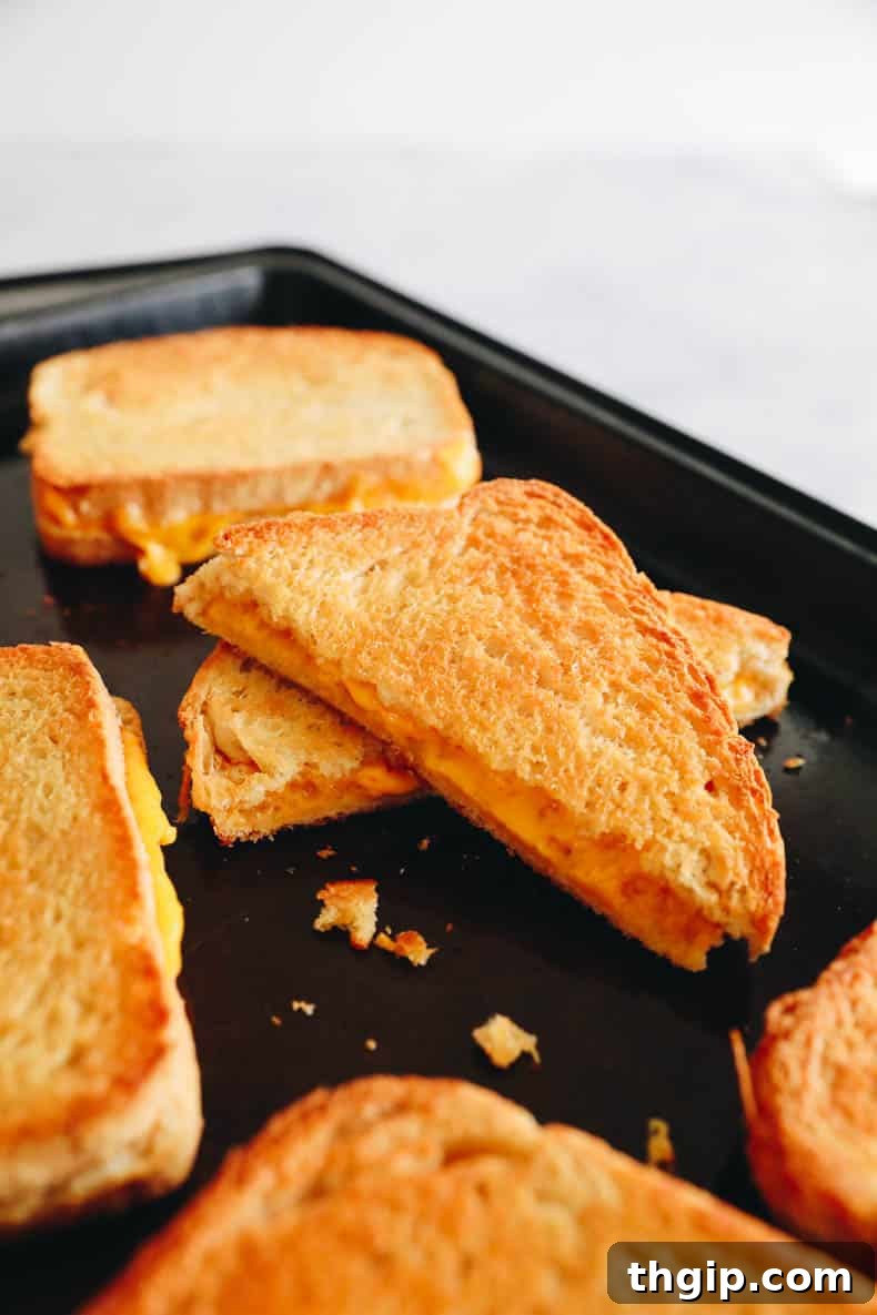 Effortless Sheet Pan Melts 6 Stacked oven grilled cheese sandwiches with melted cheese oozing out, on a wooden board.