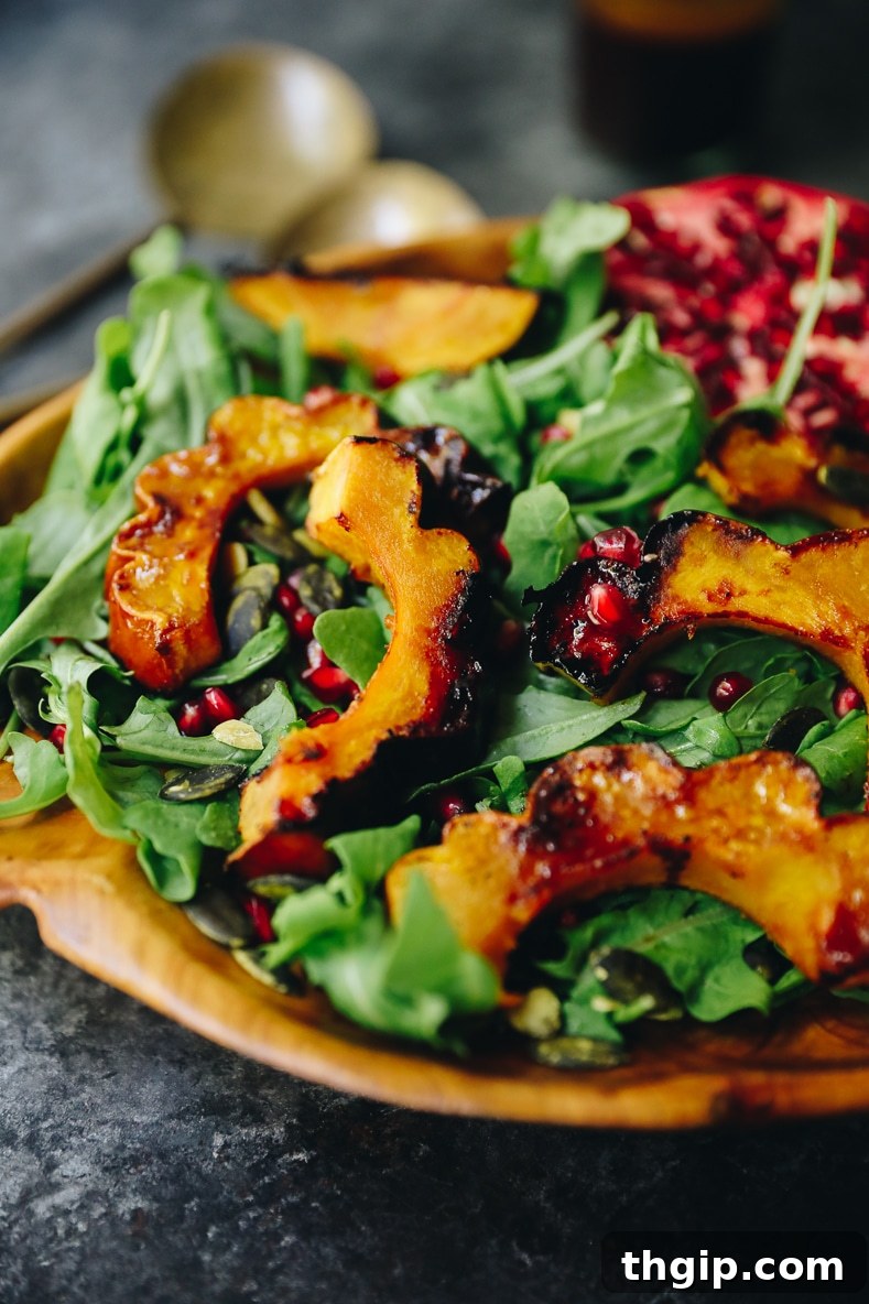 A beautifully plated maple roasted acorn squash salad with vibrant pomegranate seeds, fresh arugula, and golden squash slices, ready to be served.