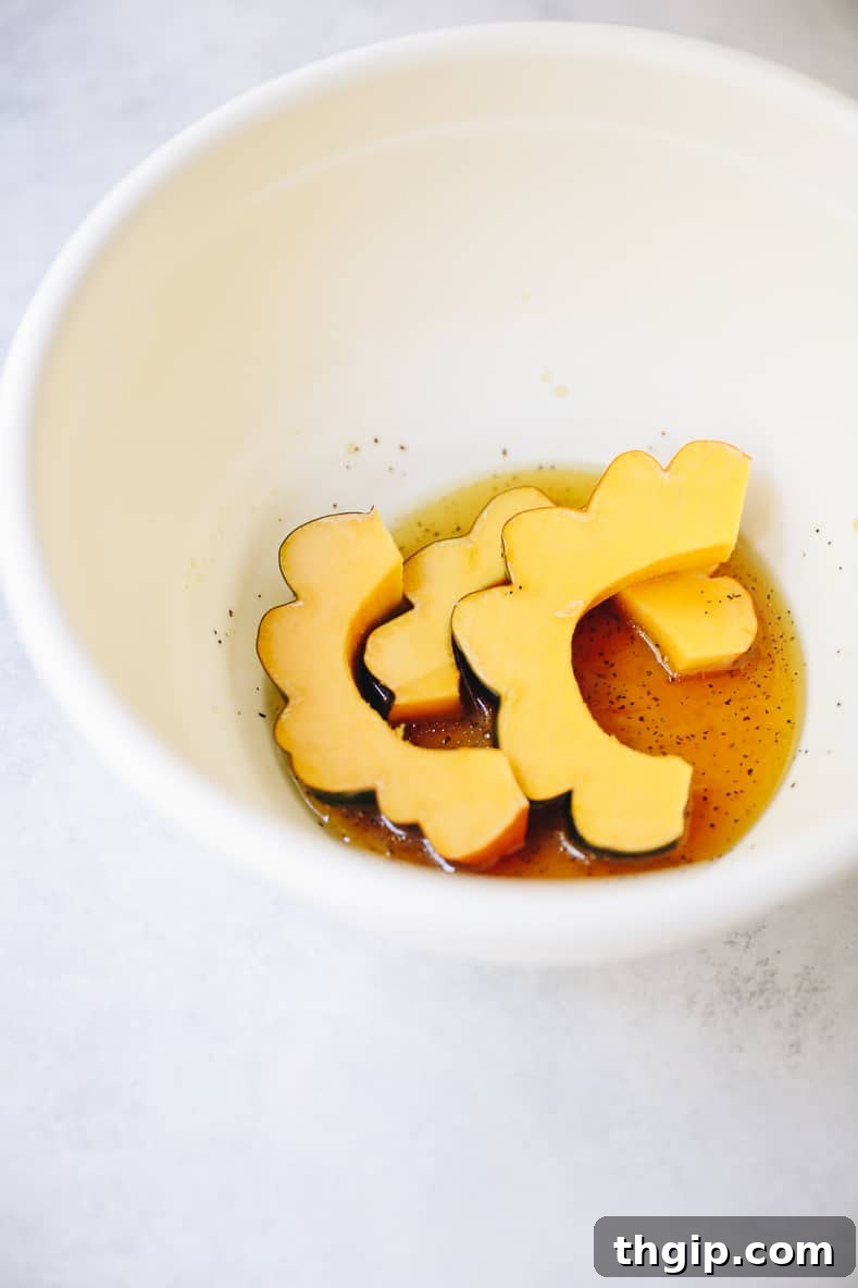 Acorn squash slices being thoroughly coated in a glossy maple syrup and olive oil mixture within a large bowl, ready for the oven.