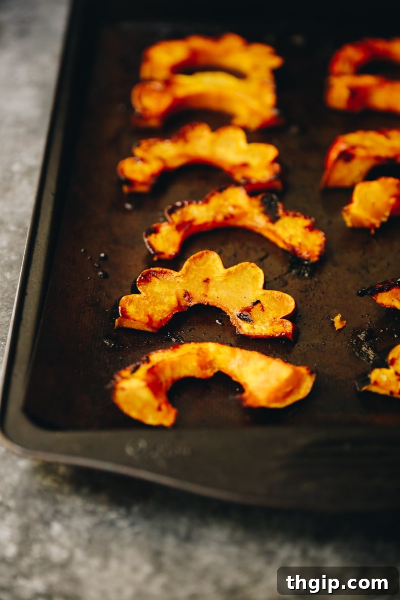 Perfectly maple roasted acorn squash slices, golden brown and caramelized, spread out on a baking sheet after cooking.