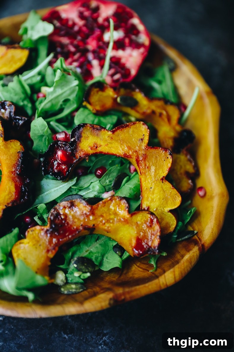 A close-up of the fully assembled fall salad, featuring maple roasted acorn squash, fresh arugula, bright red pomegranate seeds, and toasted pumpkin seeds, ready for dressing.