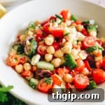 Mediterranean chickpea salad recipe in a white shallow bowl with tomatoes, cucumbers, peppers, parsley and feta.