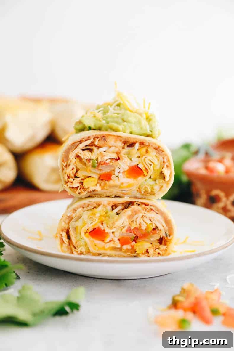 Simple Savory Chicken Burritos 2 Two halves of a chicken burrito, stacked, generously topped with fresh guacamole and shredded cheese, invitingly presented.