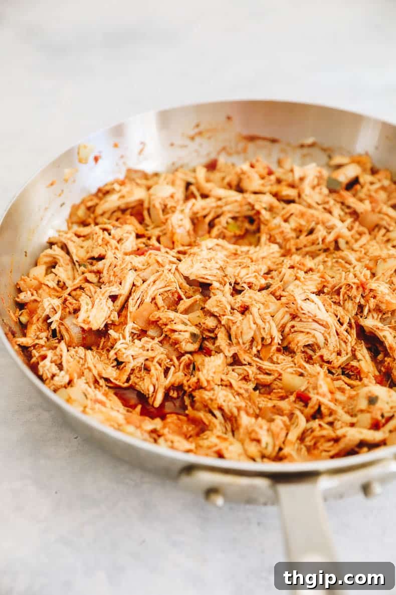 Simple Savory Chicken Burritos 3 Succulent pulled chicken simmering in a rich, spicy sauce within a pan, ready for burrito assembly.