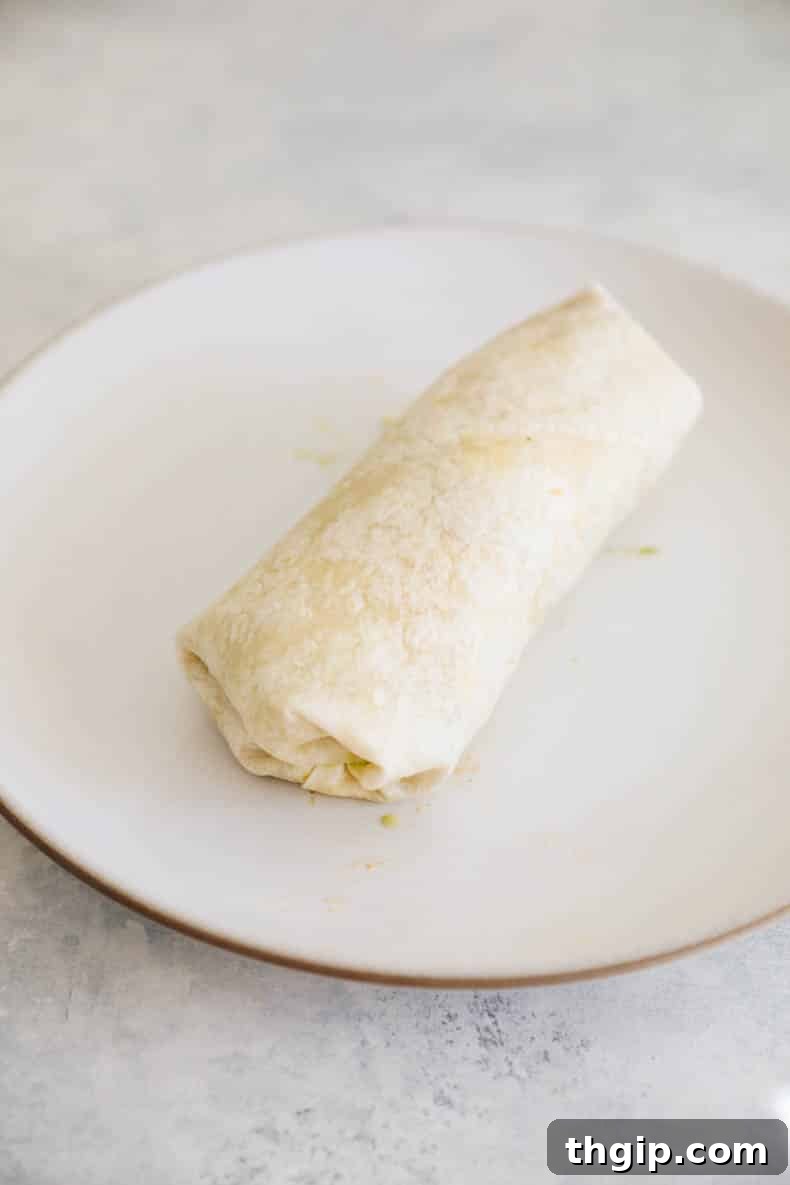 Simple Savory Chicken Burritos 7 Step-by-step image of a burrito being wrapped, showing the bottom folded up and the roll beginning.