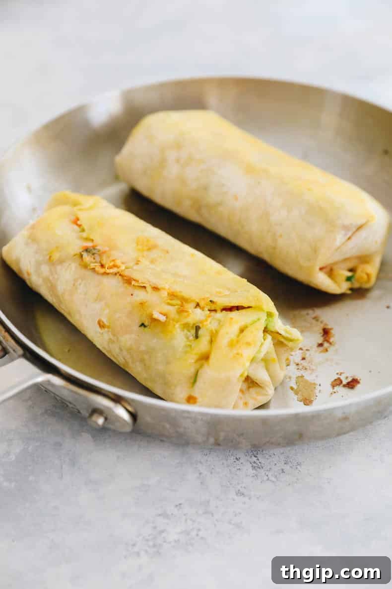 Simple Savory Chicken Burritos 8 Crispy pan-fried chicken burritos searing in a hot skillet, showcasing their golden-brown exterior.