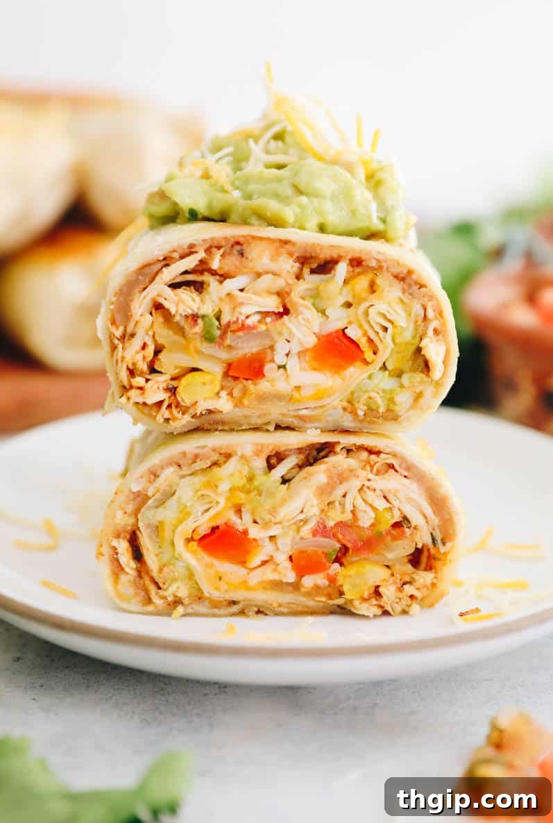 Simple Savory Chicken Burritos 9 A close-up overhead shot of a freshly assembled chicken burrito, beautifully cut in half and garnished with vibrant guacamole and a sprinkle of shredded cheese.