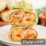 A top-down view of a chicken burrito recipe, sliced in half and served with a dollop of guacamole and shredded cheese.