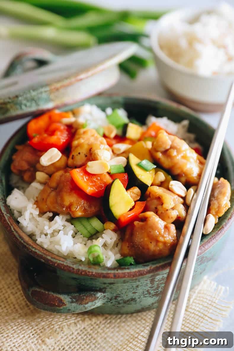 kung pao chicken over rice in a green bowl, garnished with peanuts and green onions.
