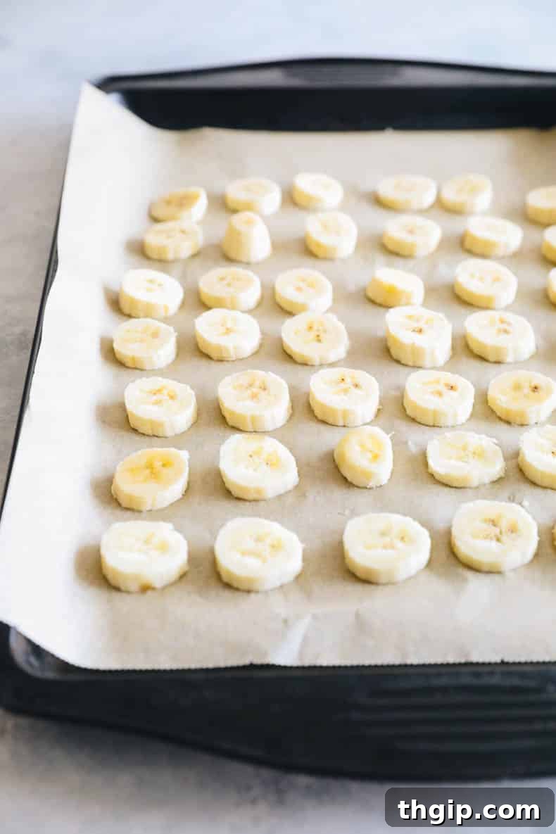A baking sheet covered with parchment paper, topped with a single layer of freshly sliced banana coins, ready for flash freezing.