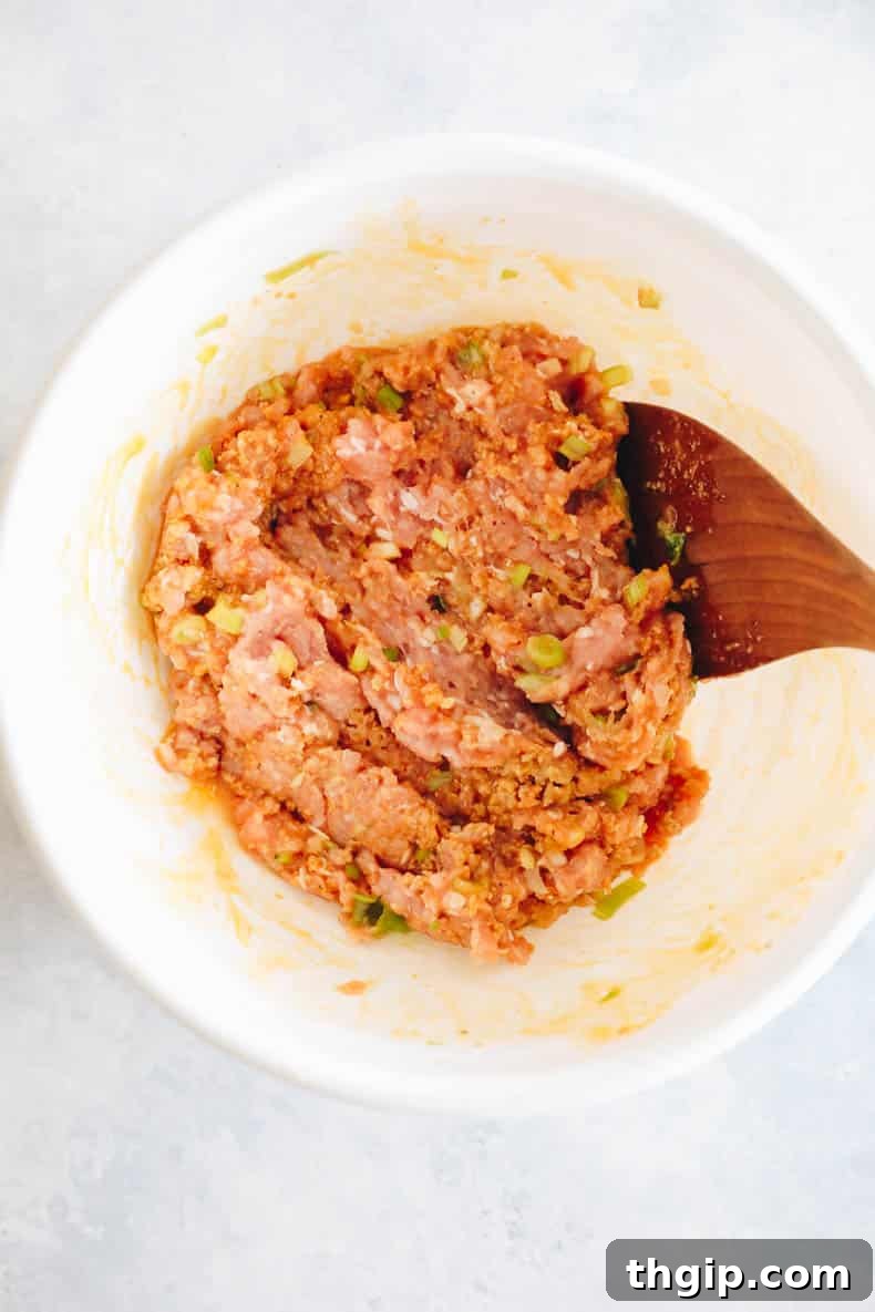 Ground chicken mixed with buffalo sauce and other seasonings in a large bowl, ready for forming into meatballs.