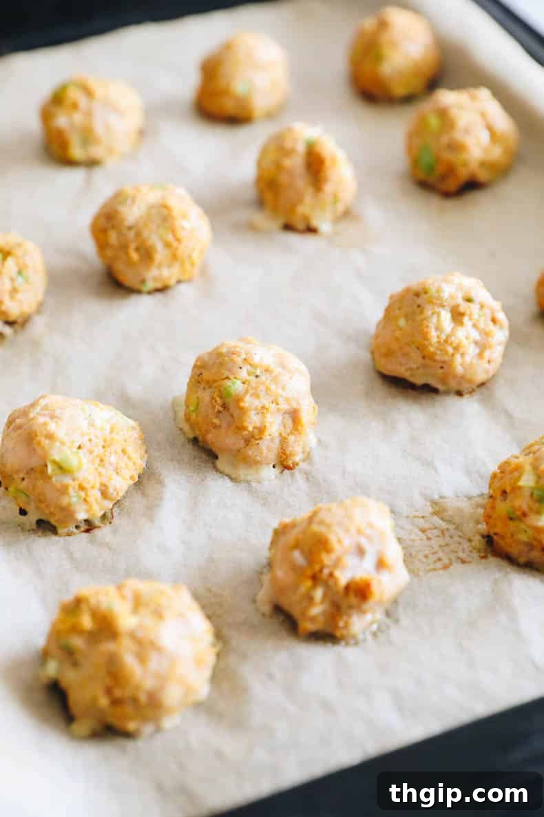 Freshly baked buffalo chicken meatballs resting on a parchment-lined baking sheet, golden brown and ready for coating.
