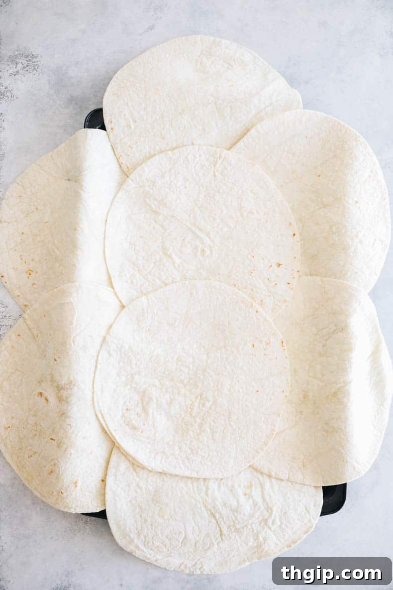 Ultimate Sheet Pan Quesadilla 3 Large flour tortillas strategically arranged on a greased sheet pan, overlapping at the edges and center to form a continuous base for filling.