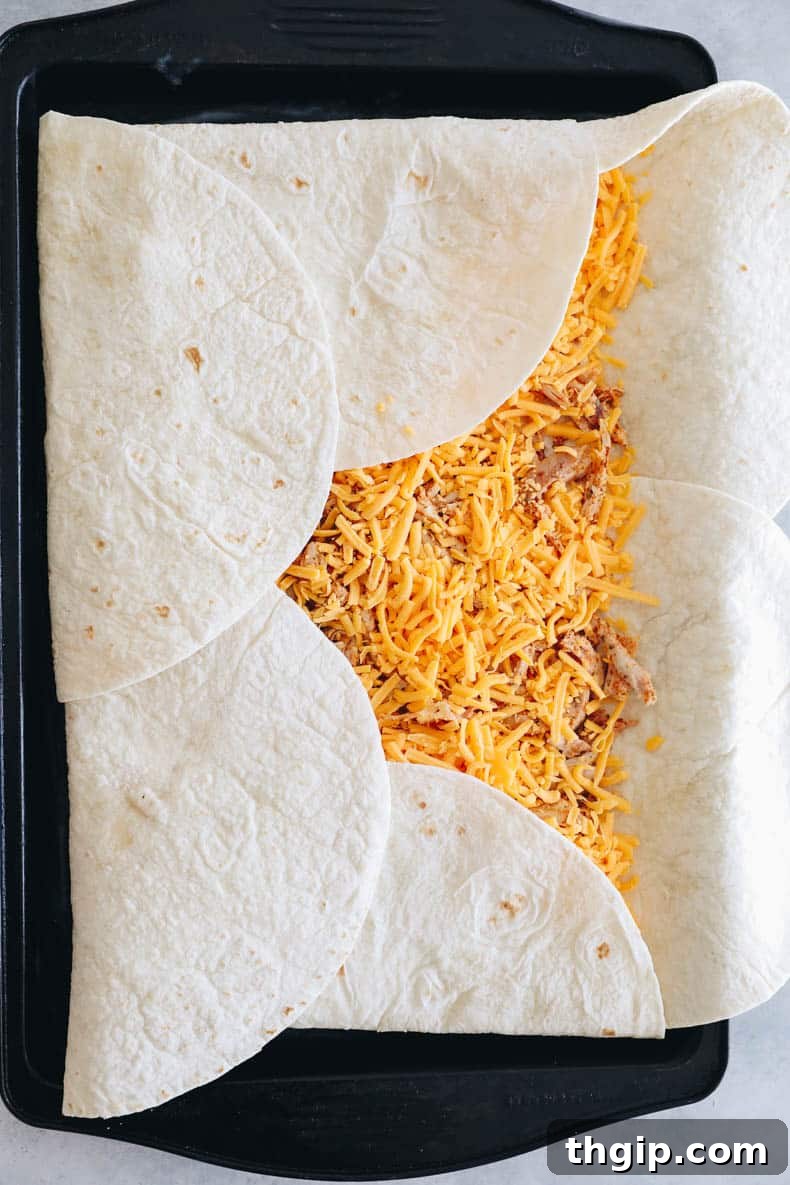 Ultimate Sheet Pan Quesadilla 5 A sheet pan filled with tortillas, chicken, and shredded cheese, before the final fold and baking process.