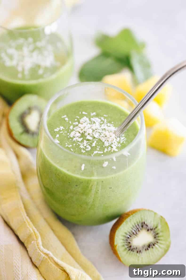 A refreshing tropical kiwi smoothie served in a clear glass with a reusable metal straw, garnished with shredded coconut for an extra touch of tropical flair.