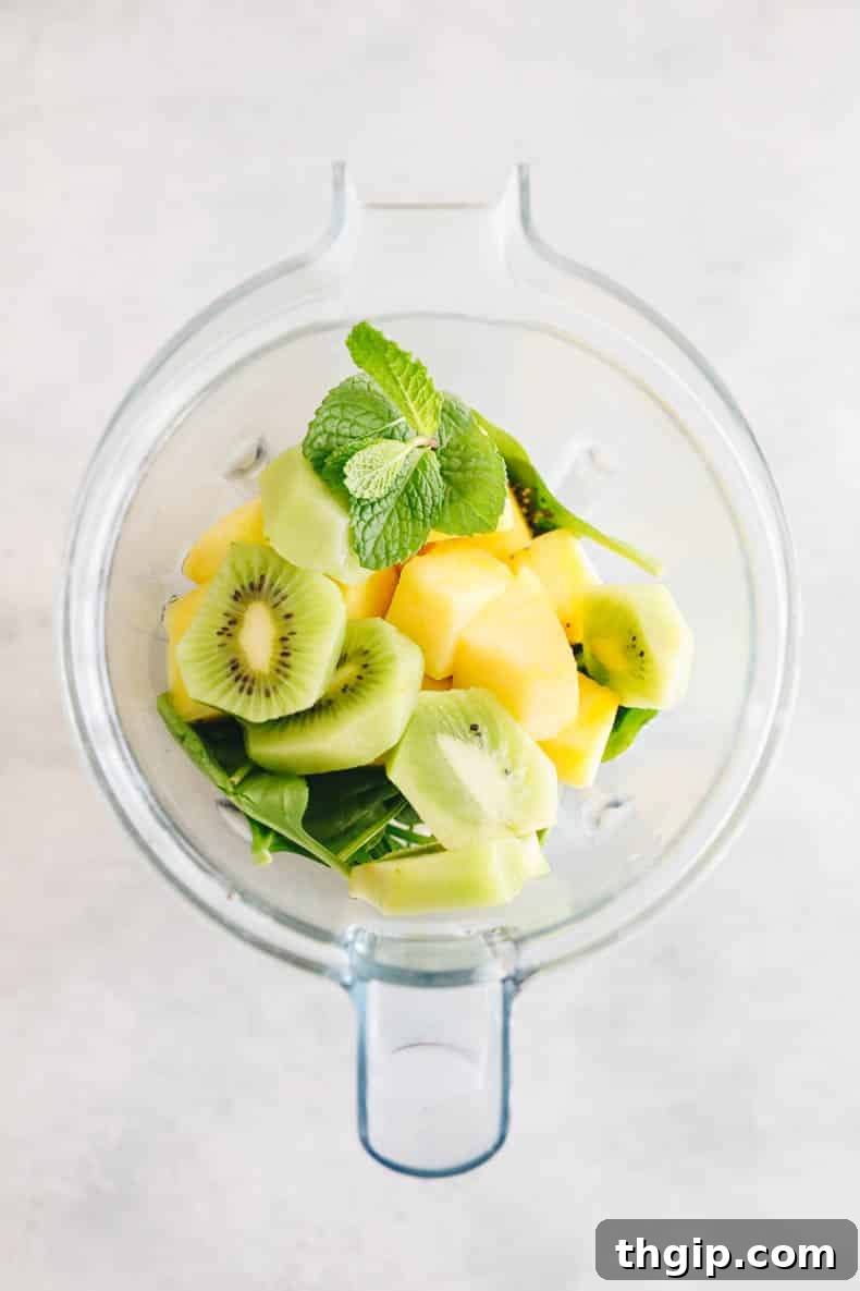 A high-angle shot showcasing fresh ingredients for a tropical kiwi smoothie: vibrant green kiwis, juicy pineapple chunks, aromatic mint leaves, and a handful of nutrient-dense spinach leaves, all ready to be blended.