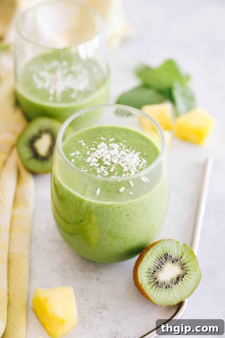 Two clear glasses filled with vibrant green tropical kiwi smoothie, garnished with fresh mint leaves, resting on a clean white surface, ready to be enjoyed.