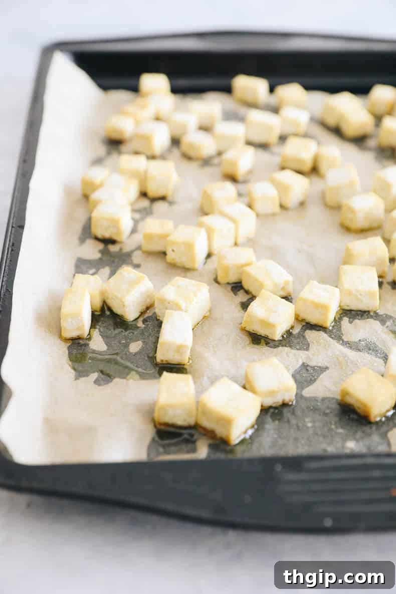 Cubed extra-firm tofu baking on a parchment-lined sheet pan, browning around the edges.