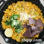Mexican Street Corn Dip in a cast iron skillet with cilantro, cotija cheese, blue corn chips + lime