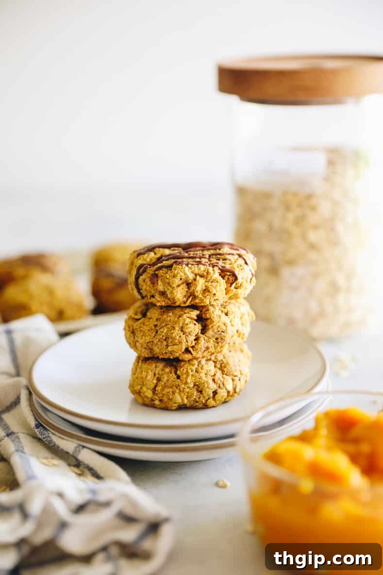 Straight on shot of a stack of pumpkin breakfast cookies on a white plate. Bowl of pumpkin in the foreground and jar of oats in the background.