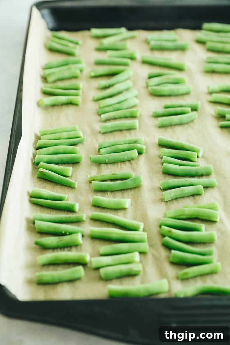 Individually frozen green bean pieces spread in a single, even layer on a parchment-lined baking sheet, ready for final packaging.