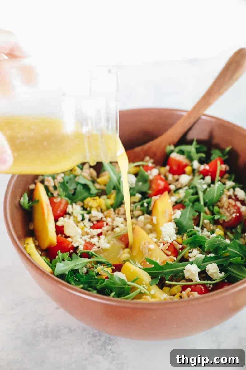 Vibrant Summer Farro Bowl 5 a hand pouring the homemade lemon vinaigrette over the vibrant farro salad in a large bowl