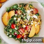 An overhead view of a vibrant summer farro salad, rich with peaches, feta, cherry tomatoes, and fresh arugula, beautifully arranged in a serving bowl.