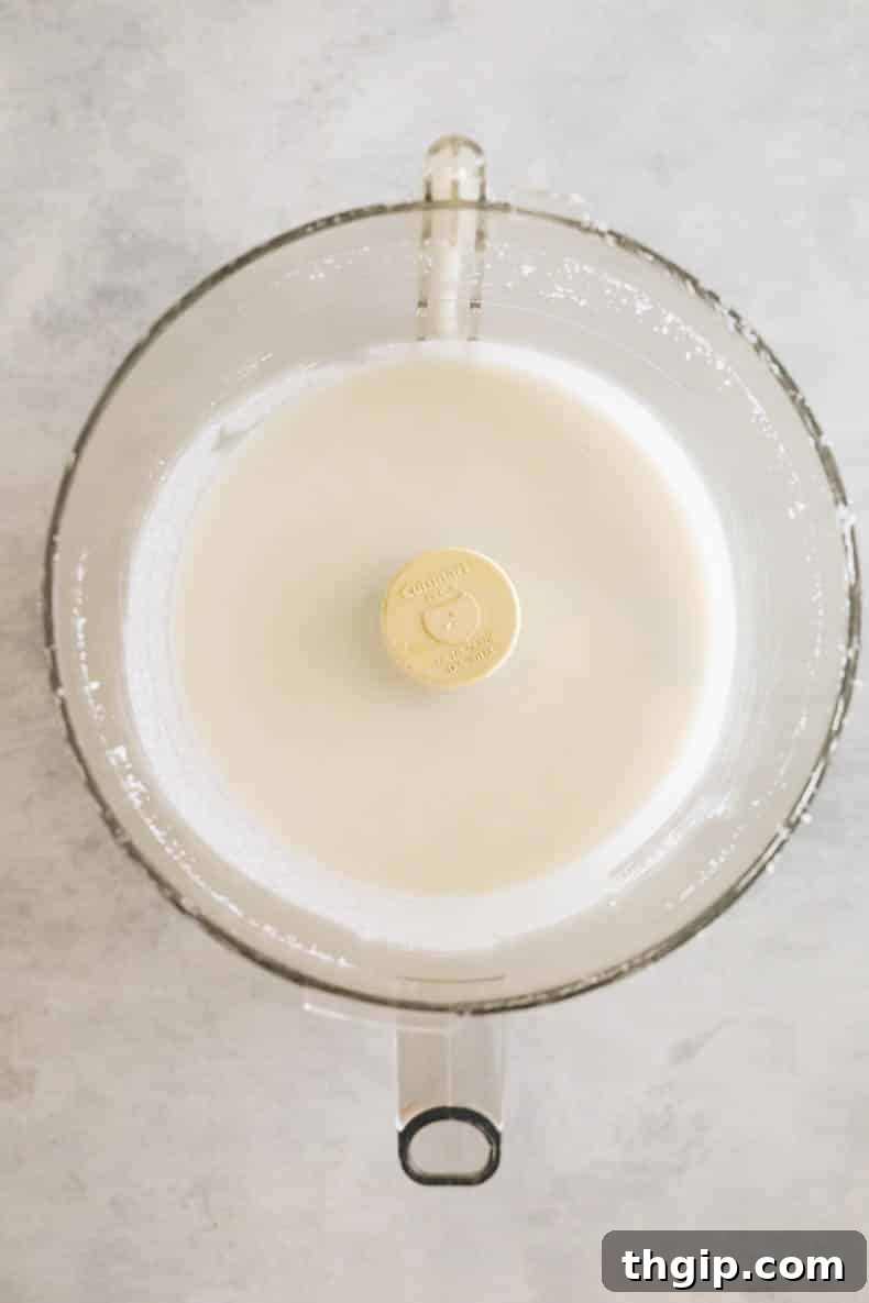 Processed coconut butter transitioning from flakes to a smooth paste in a food processor bowl.