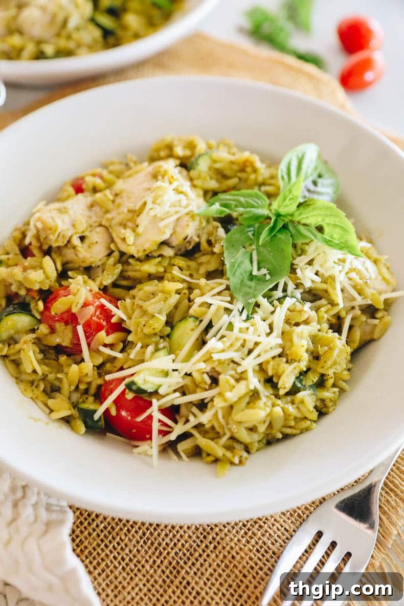 one pot pesto chicken and orzo in a white bowl, garnished with fresh basil