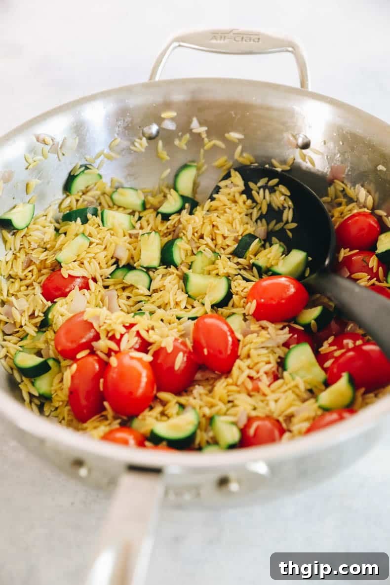 orzo pasta, tomatoes, and zucchini sautéing together in a pot