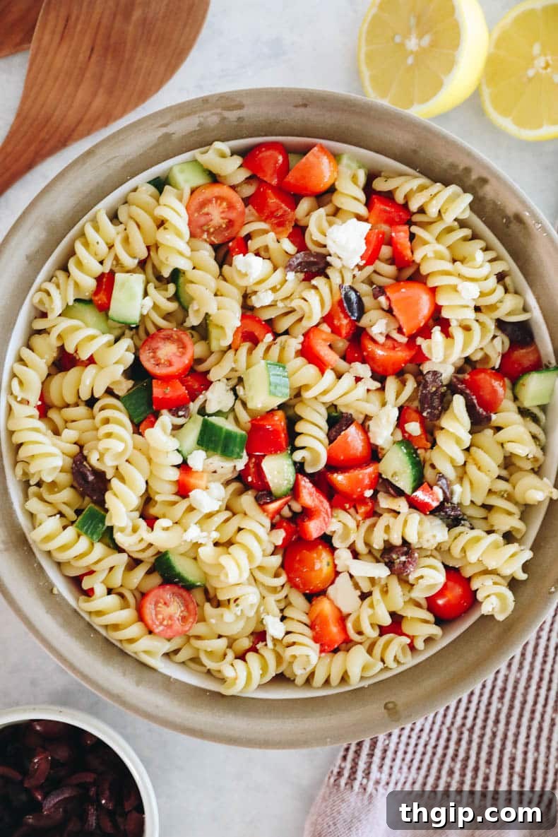 Mediterranean Pasta Delight 2 Vibrant Greek pasta salad with chunks of feta, cherry tomatoes, crisp cucumber, colorful bell peppers, and Kalamata olives, all tossed together in a large bowl.